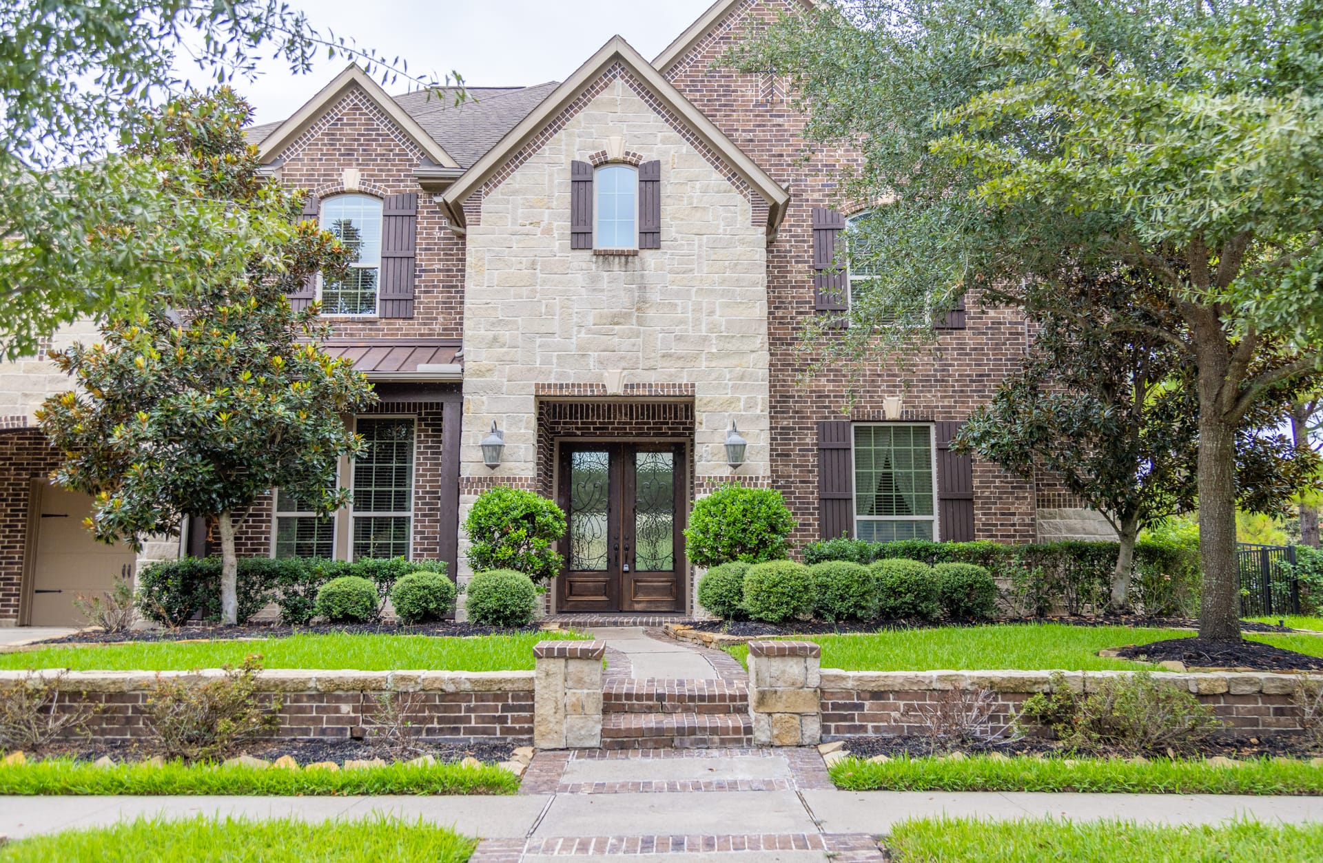 A simple and elegant modern front yard with shaped hedges, a beautiful hardscape pathway, and large shade trees.